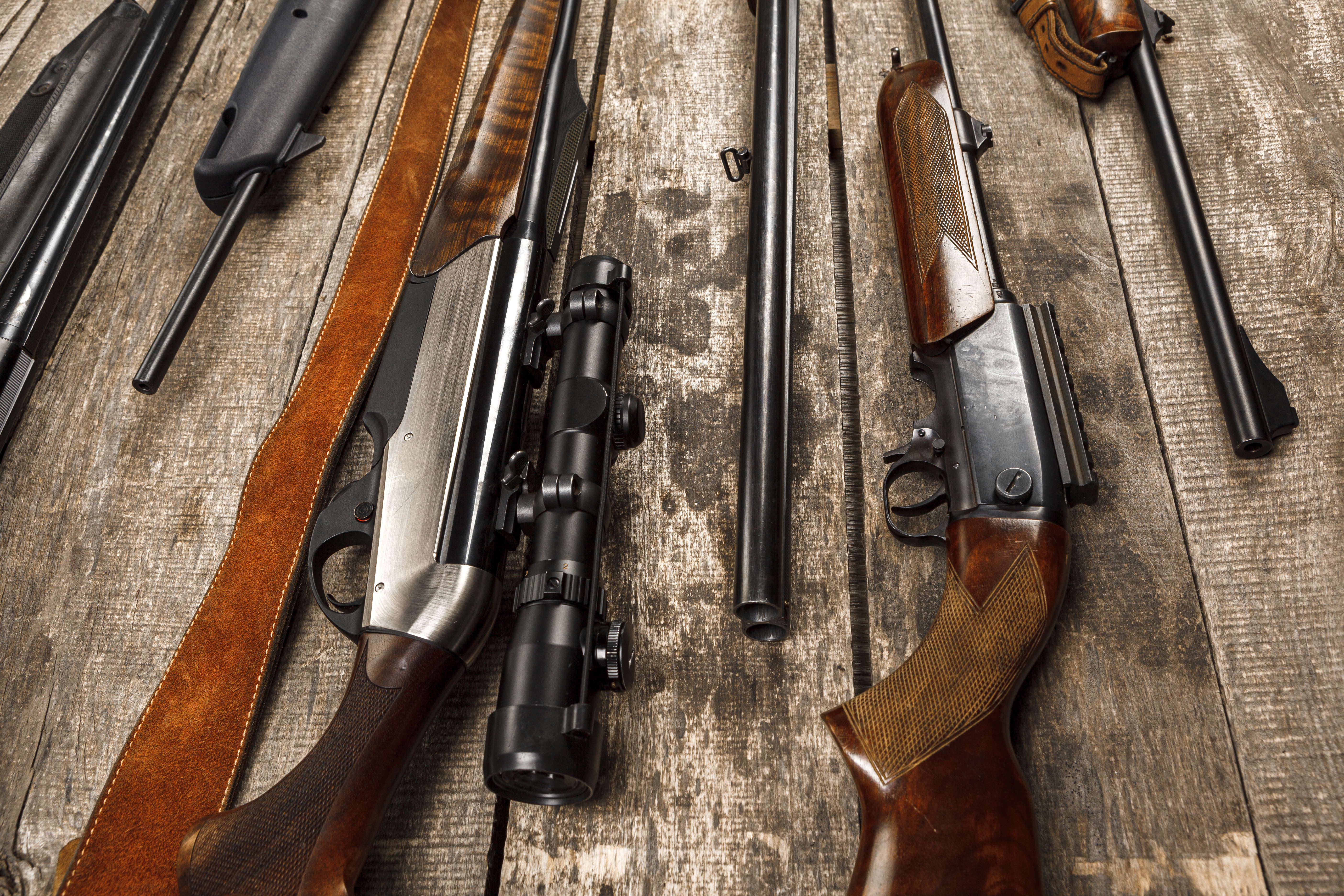 Hunting rifles, spare barrels and a leather sling laid out flat on a weathered wooden bench