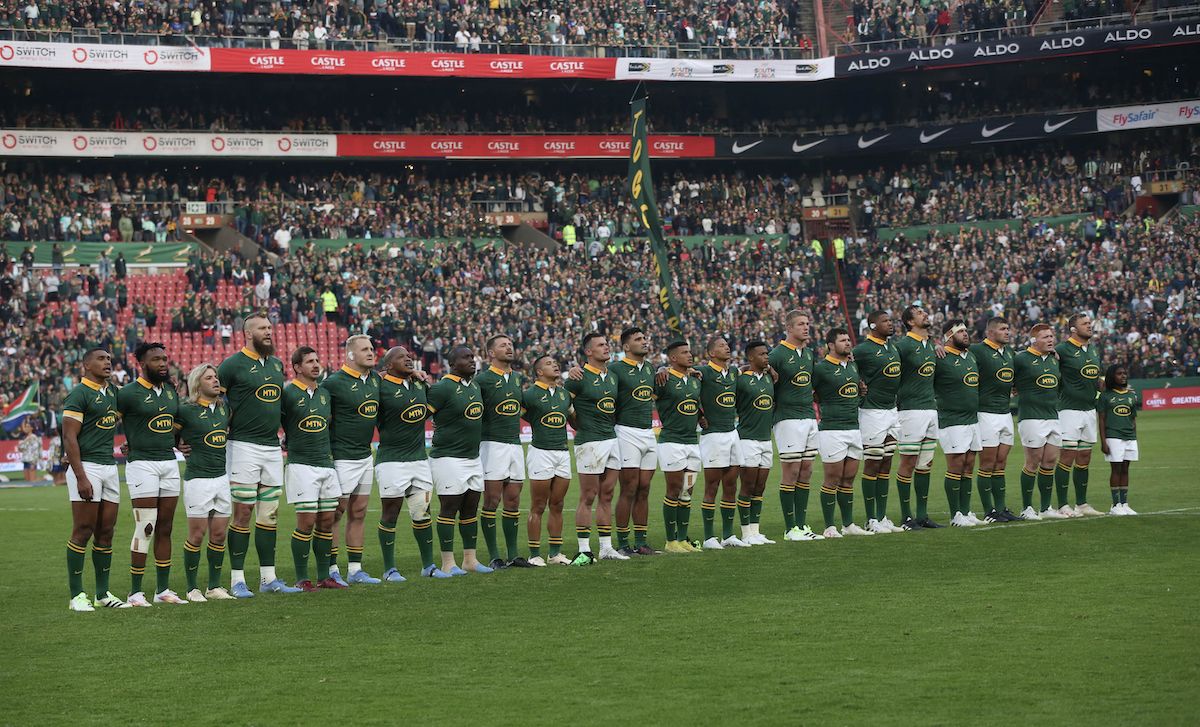 A rugby team standing in a line across the pitch for the anthem, a full stadium behind them