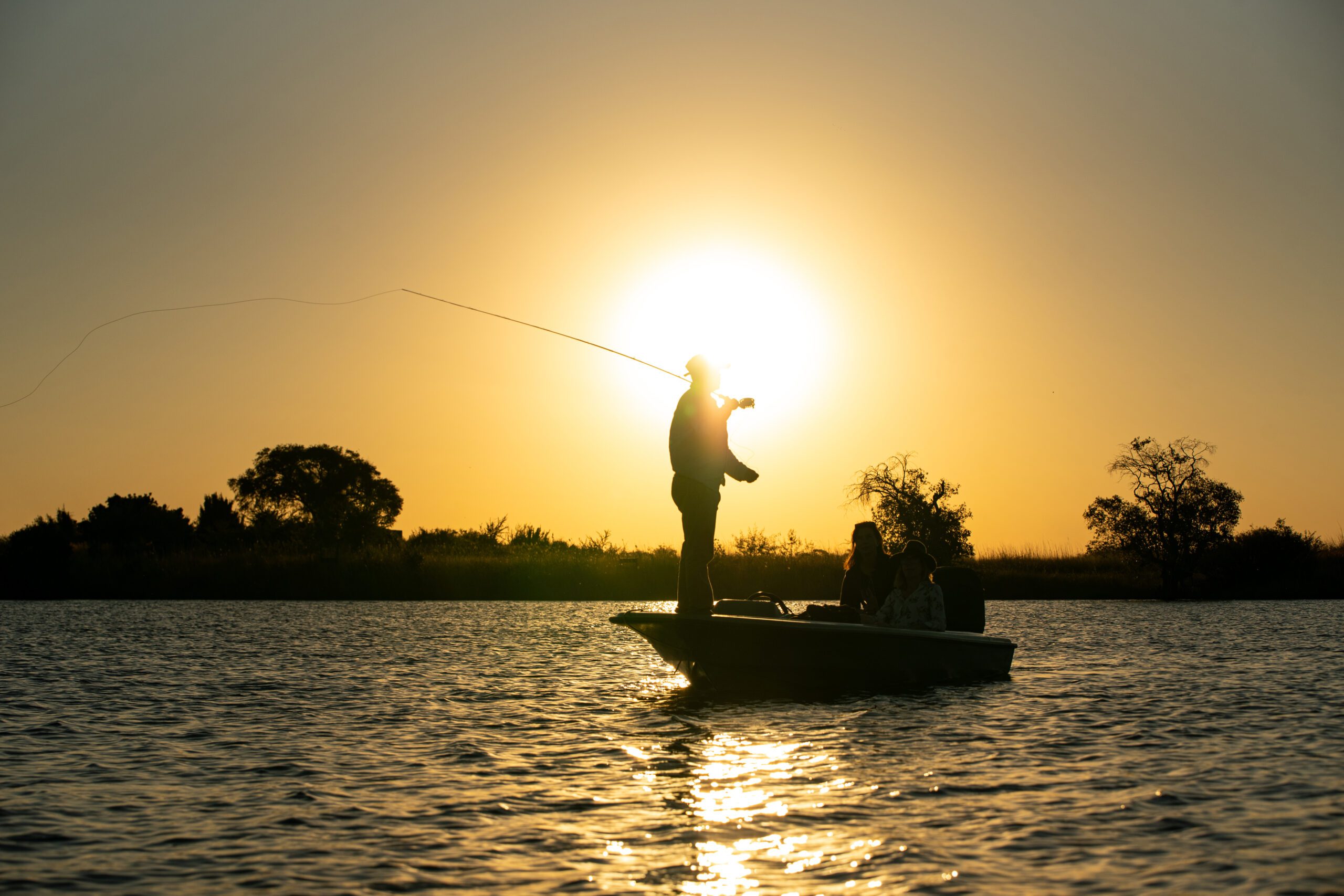 An angler casting from a boat on the Zambezi at sunset, the low sun behind the line